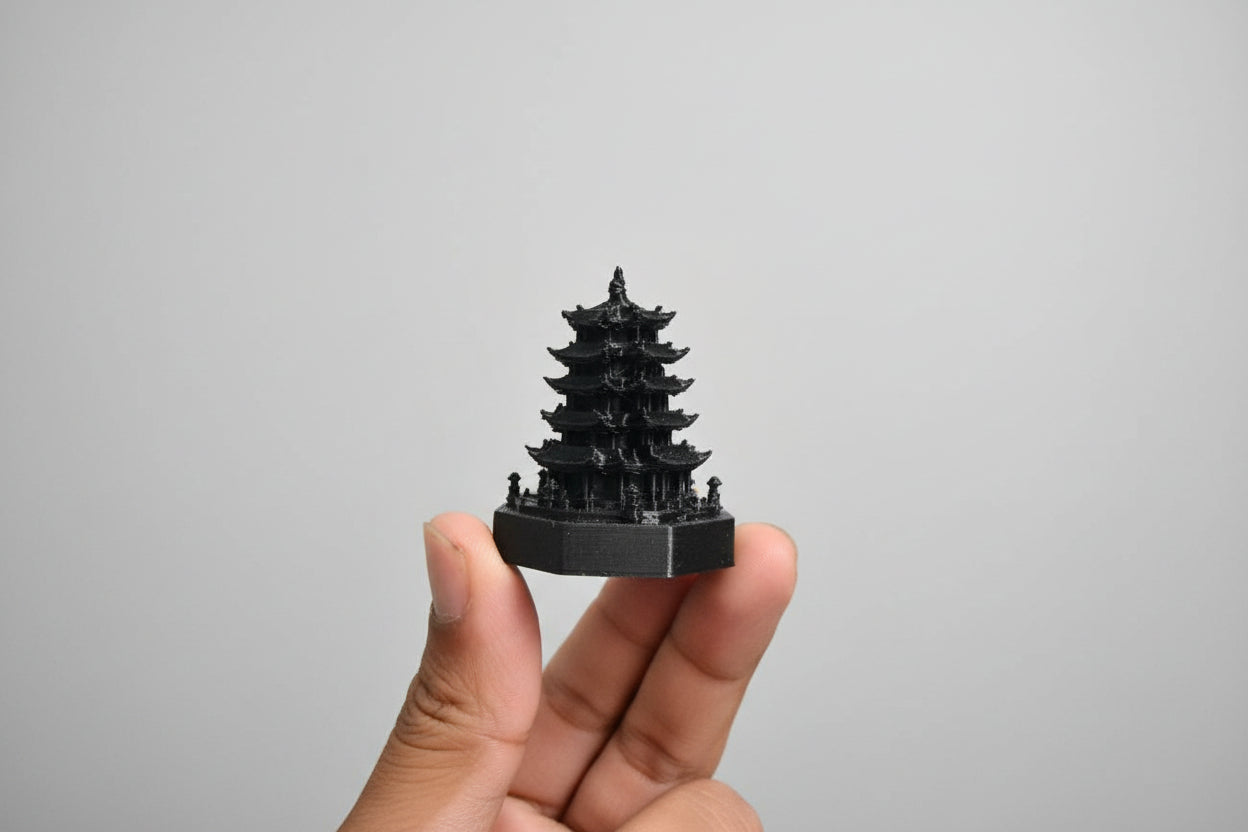 Black 3D-printed model of a pagoda held in a hand against a neutral background