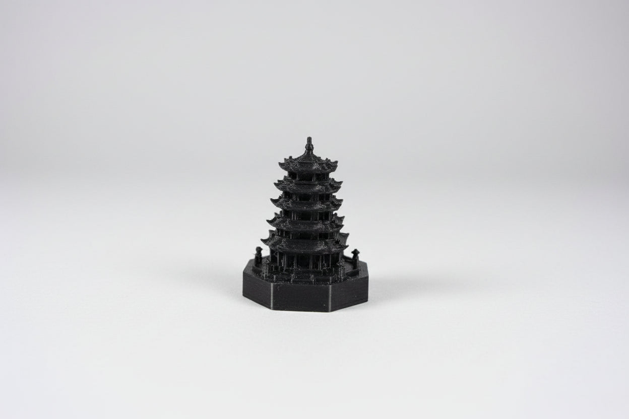 Hand holding a small black 3D-printed model of a pagoda against a plain background